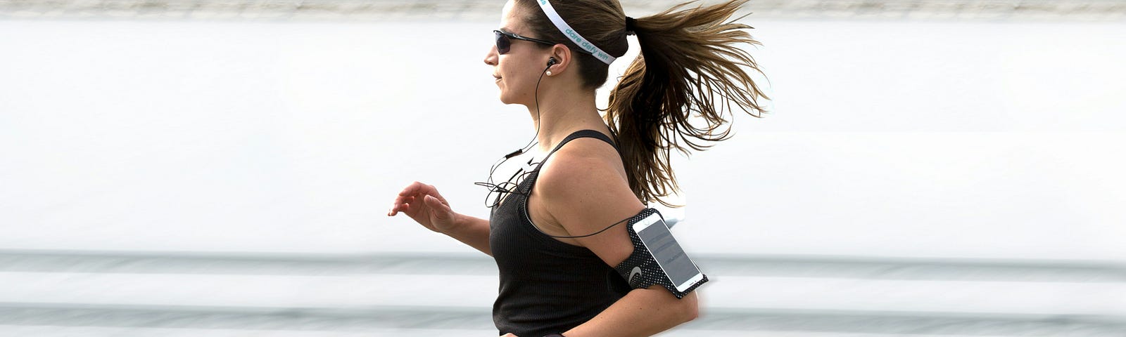 woman jogging in a black top and black leggings while listening to music.