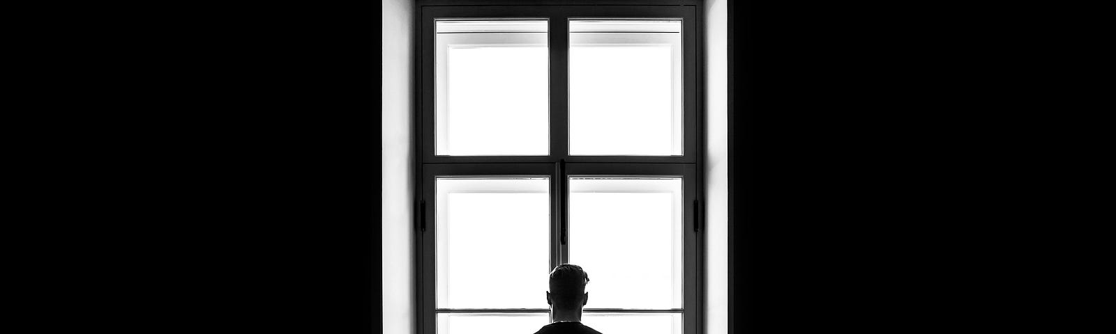 lone figure standing in front of a windowpane