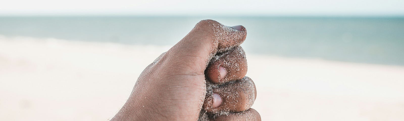 a hand sifting sand on a beach