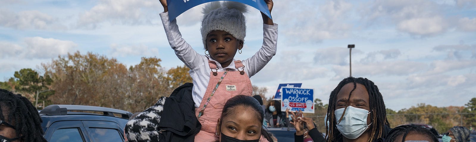 A child holding a sign sits on the shoulders of a young woman