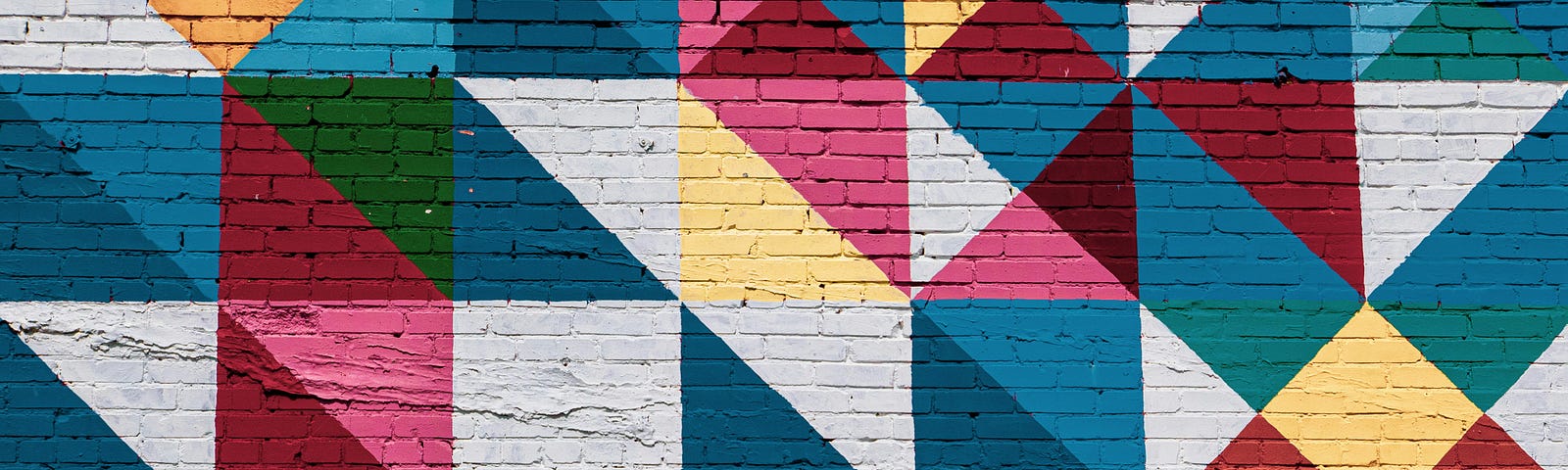 paint on a brick wall in a quilt pattern of blues, pinks, greens, yellows, whites and black