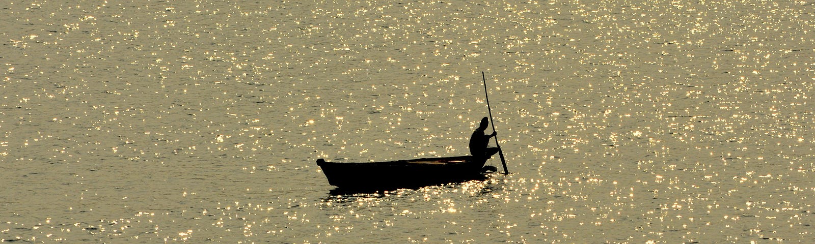 A person in a boat, silhouetted against a golden glittering ocean