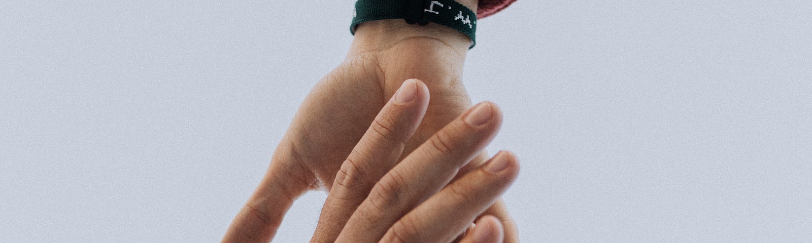 One hand with a black bracelet reaching down to grab a man’s hand with a beaded bracelet.