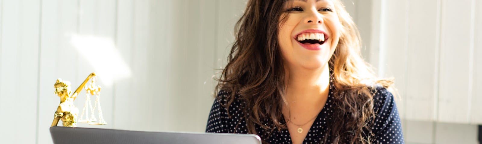 A woman laughing while working in front of a laptop