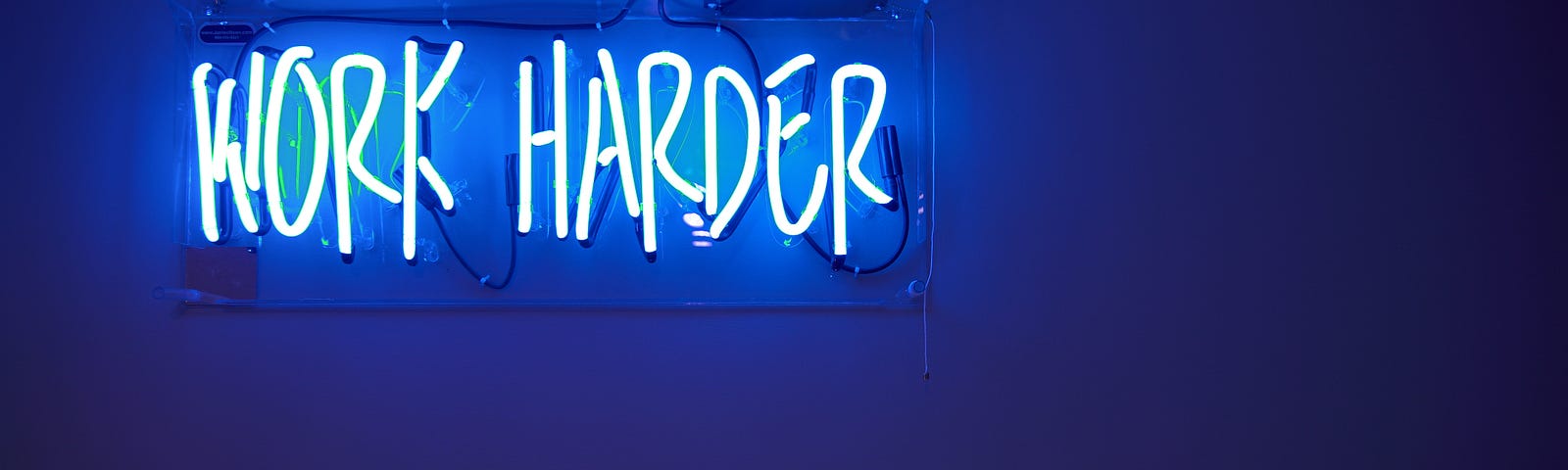 Neon Sign in Blue reading, “Work Harder”