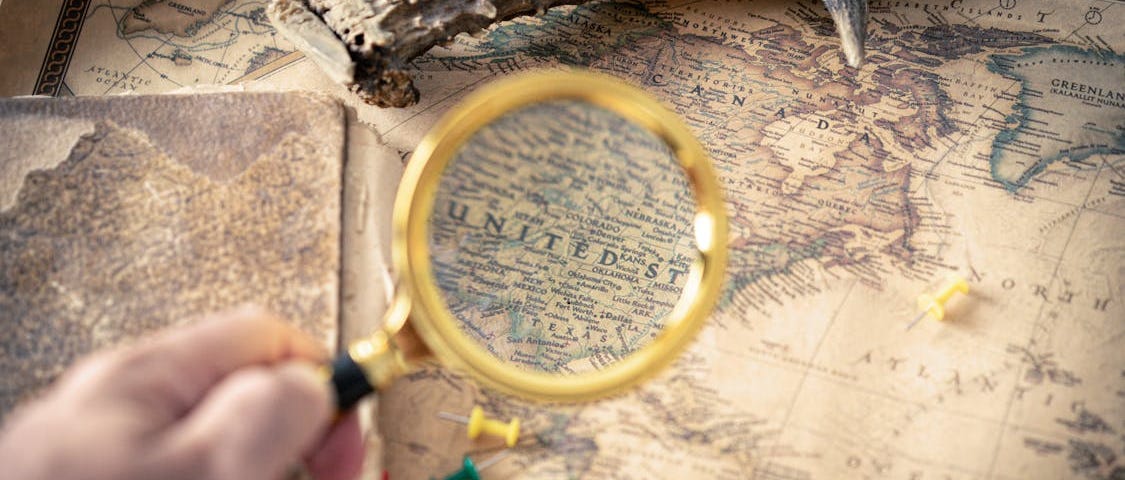 Person holding a magnifying glass over a map.