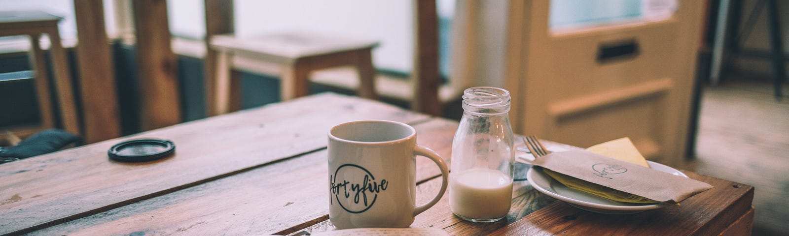 Coffee cup next to open journal with pen on rustic wood table.