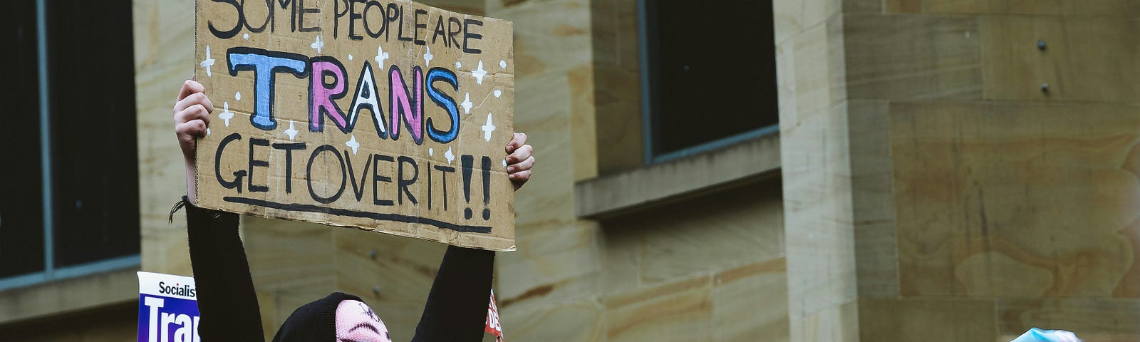 A protestor holding a sign that says some people are trans, get over it