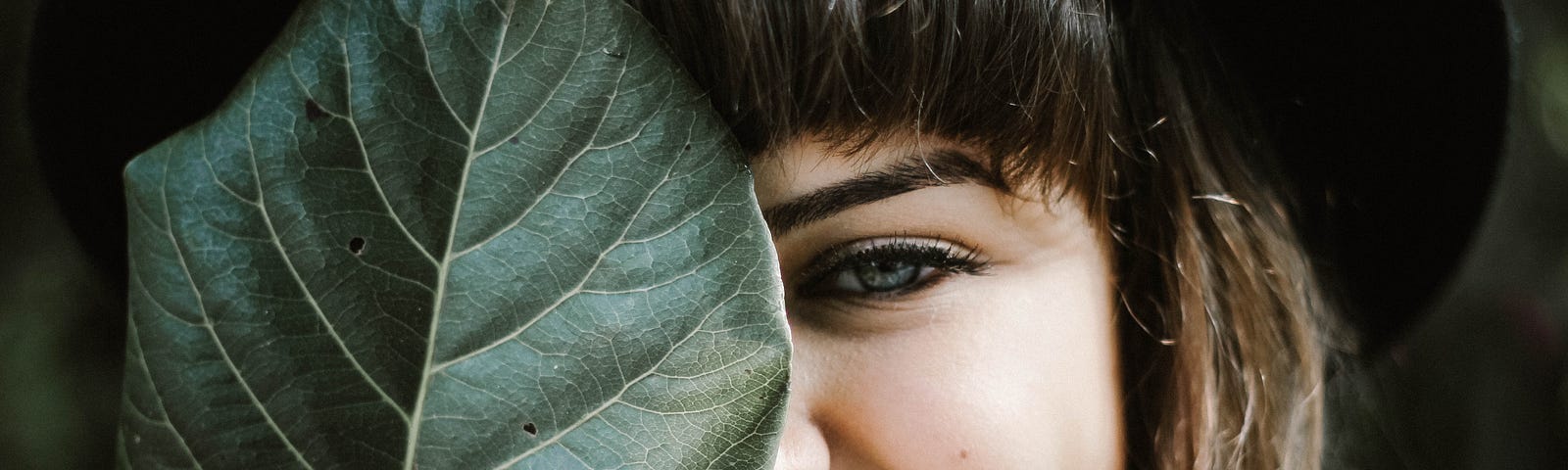 Beautiful woman smiling, covering half her face with a leaf.