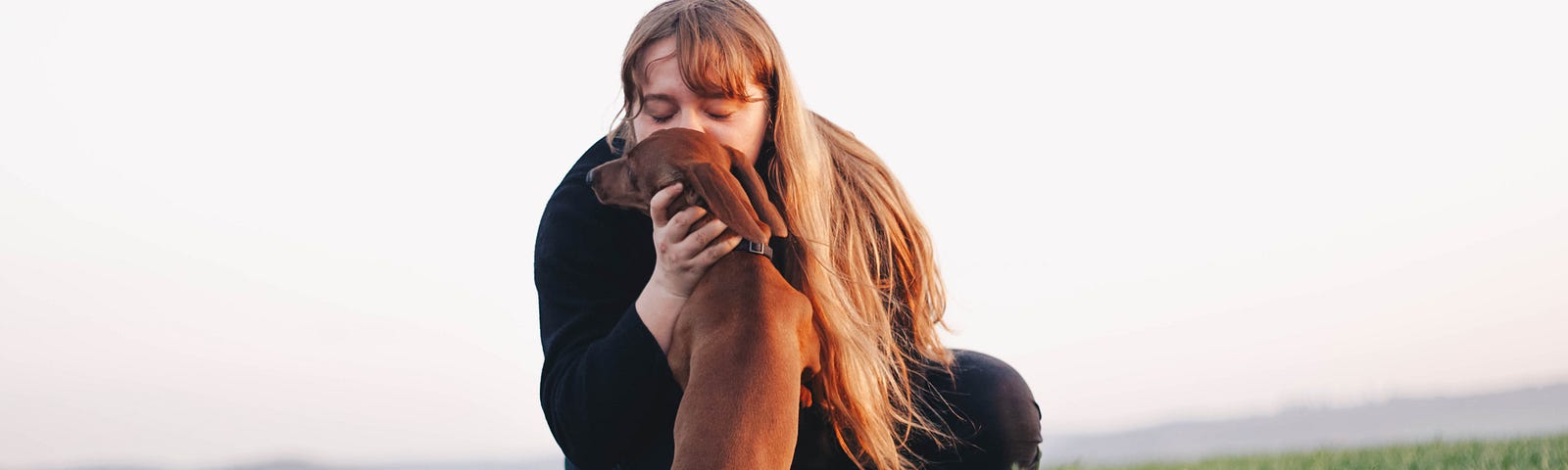 Lady kissing a dog in a green field