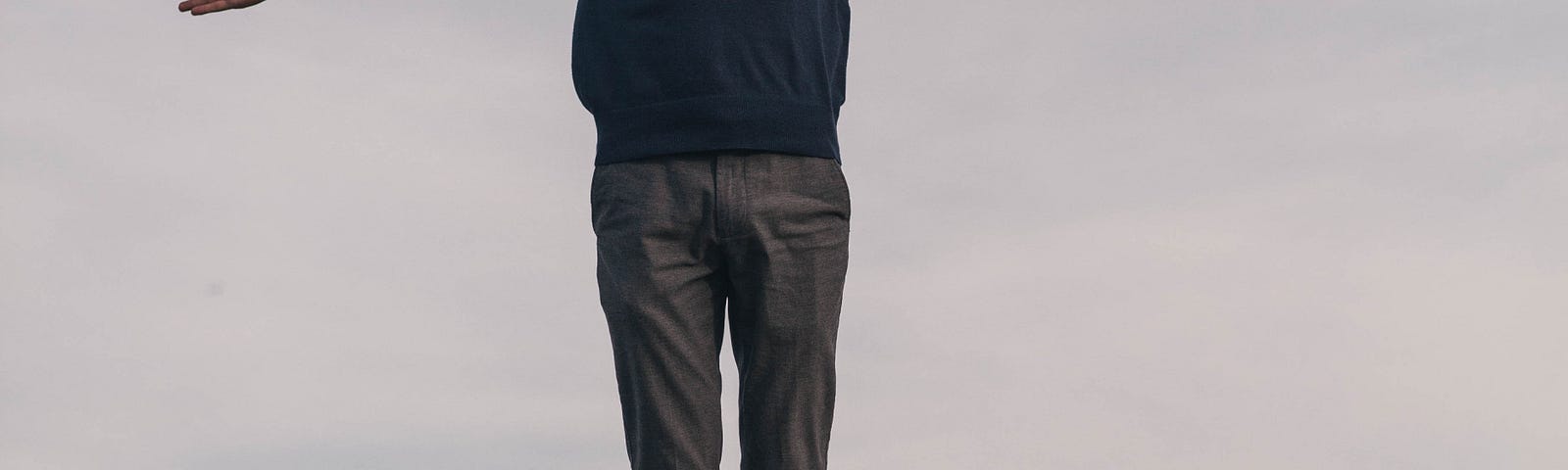 A white male seeming levitates (arms out) a couple feet over a rock.