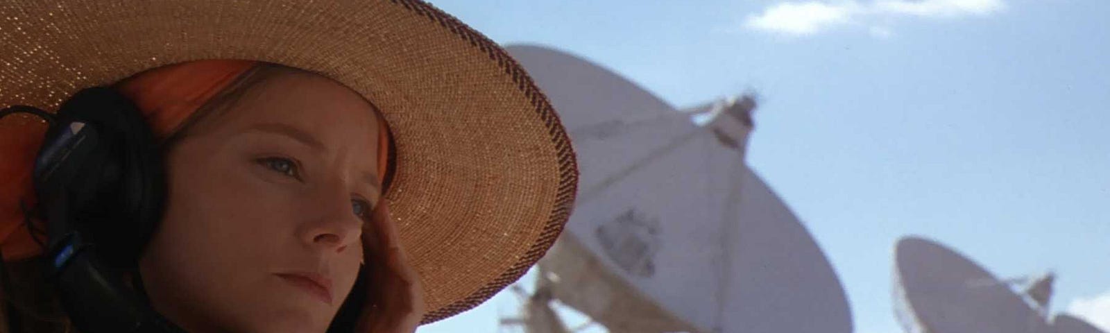 Jodie Foster’s Ellie Arroway sits in front of the Arecebo Radio Telescope observatory in the film Contact, with headphones