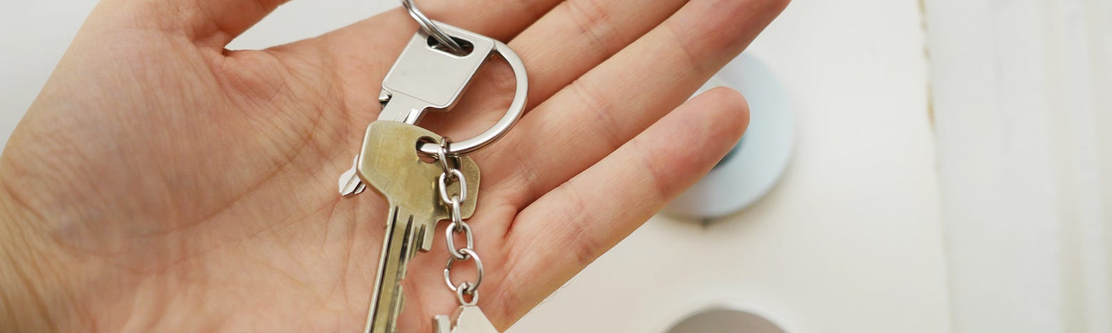 A person holding a set of house keys cupped in their palm. The closed, locked door of a house makes up the background.