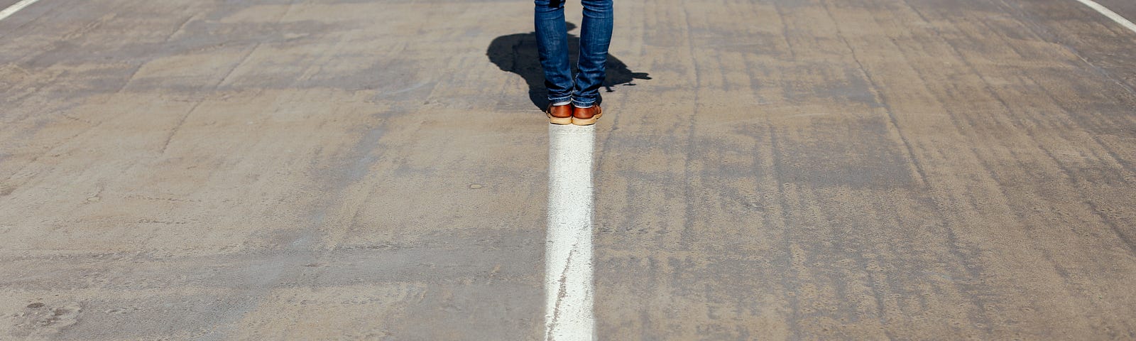 Jeans-clad man, seen from the waist down at the image top, walks away from us. There is a painted white arrow that points back at us, beginning at his feet.