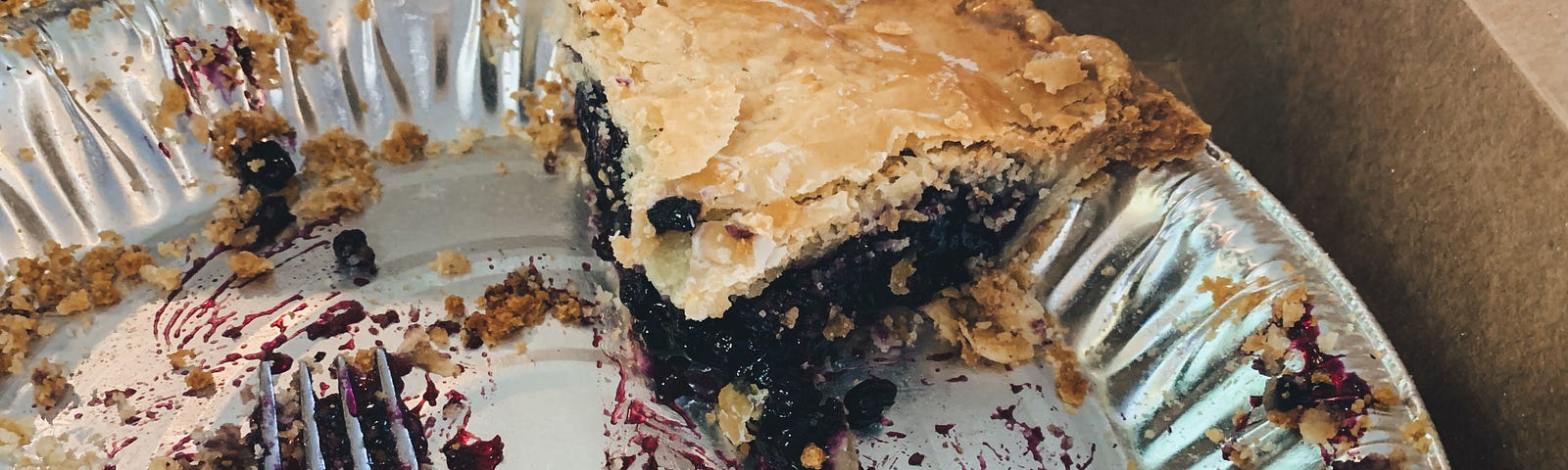 aluminum pie pan with one slice of blueberry pie remaining along with a dirty fork