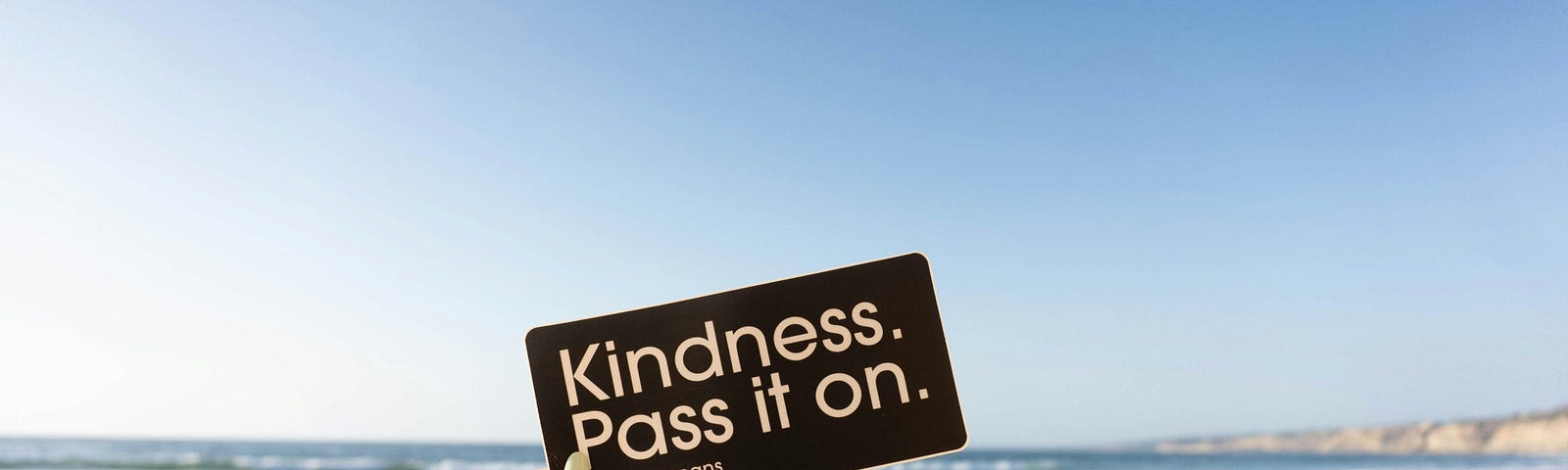 A woman’s hand holding a black card with the message “Kindness. Pass it on.”