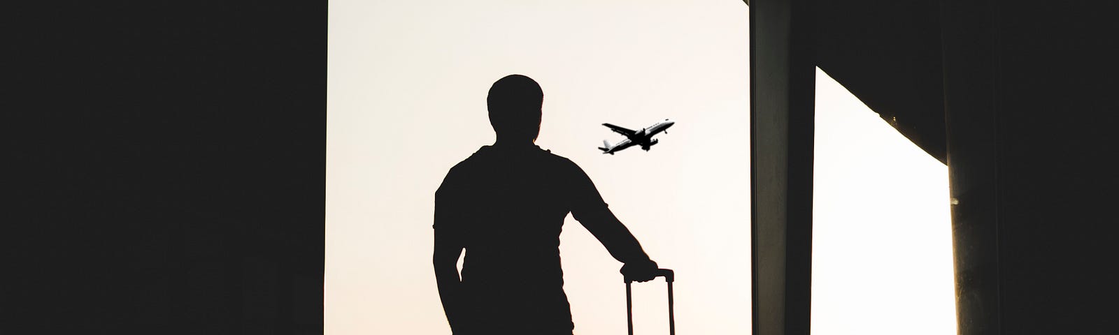 silhouette of a traveler looking out a window at a plane in the airport.