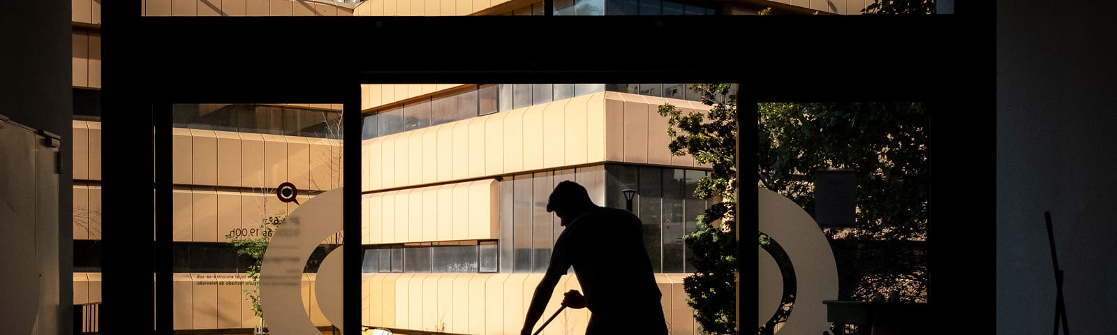 Janitor mopping the sidewalk in front of a building in the business district. Other cleaning tools are behind him, inside.