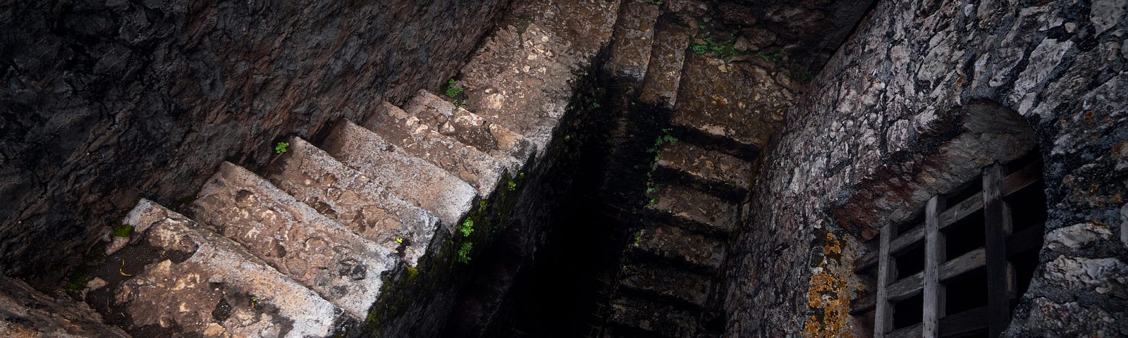 An old, stone staircase goes down past a window covered with iron bars into the darkness of an ancient prison.