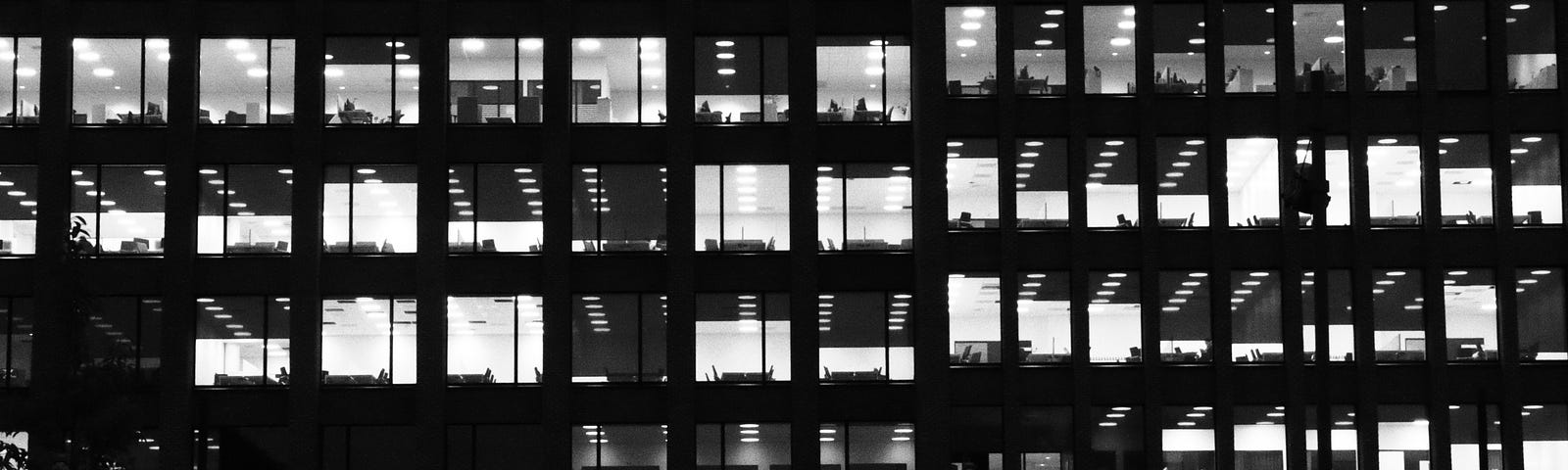 Image of an office building with large glass windows and lights on in some