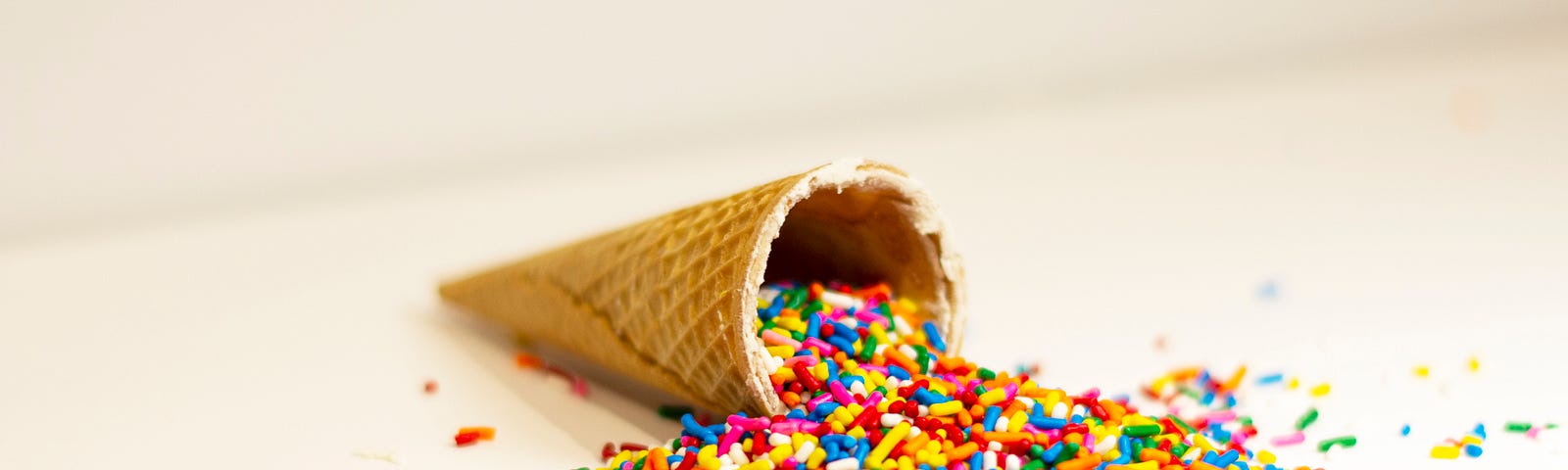 An icecream cone on its side, with lots of sprinkles (100’s & 1000’s) spilling out onto the woirksurface.