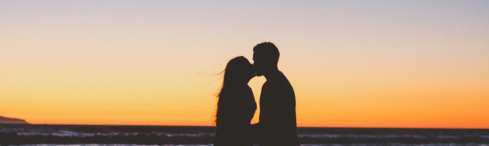 Couple kissing on the beach at sunset.