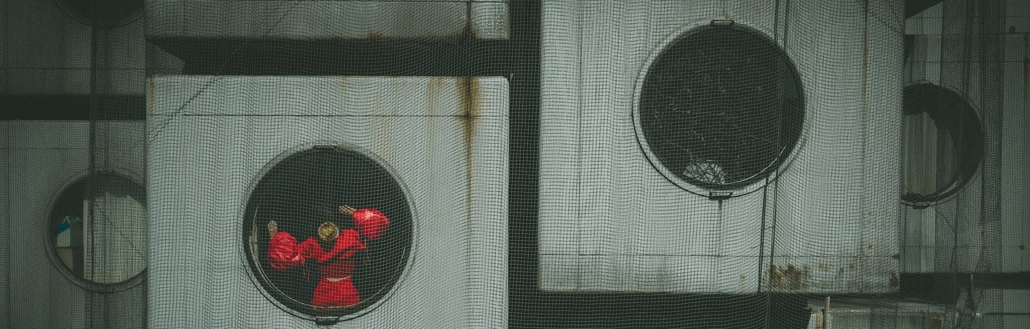 person in red looking out of dystopian cement block with windows