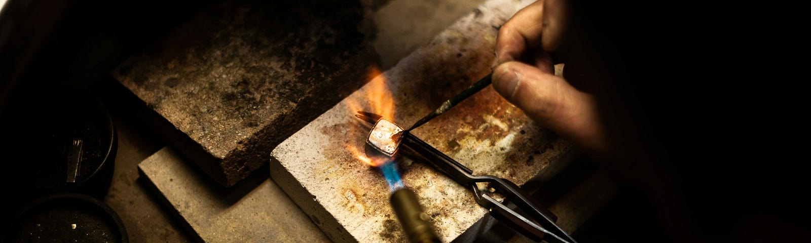 An artisan making jewelry on a small stone slab with wire and pliers and hot torch.