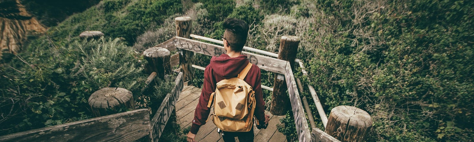 A person with a backpack walks down a wooden staircase surrounded by lush greenery, symbolizing the journey of taking steady, mindful steps towards achieving goals.