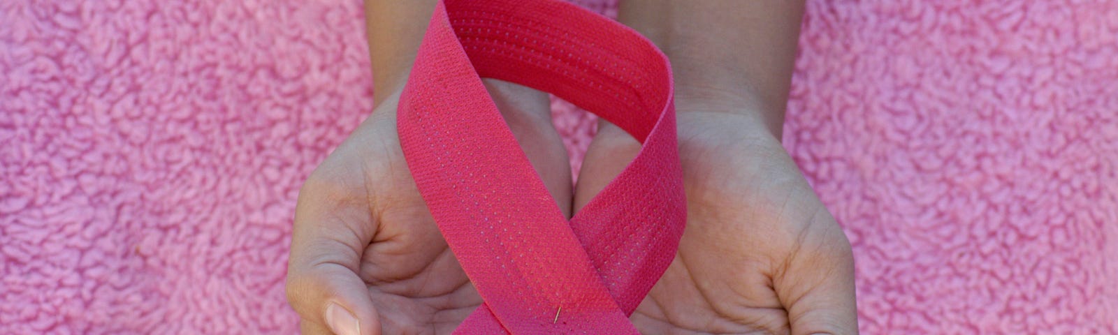 A woman holds a breast cancer ribbon against a fluffy pink blanket