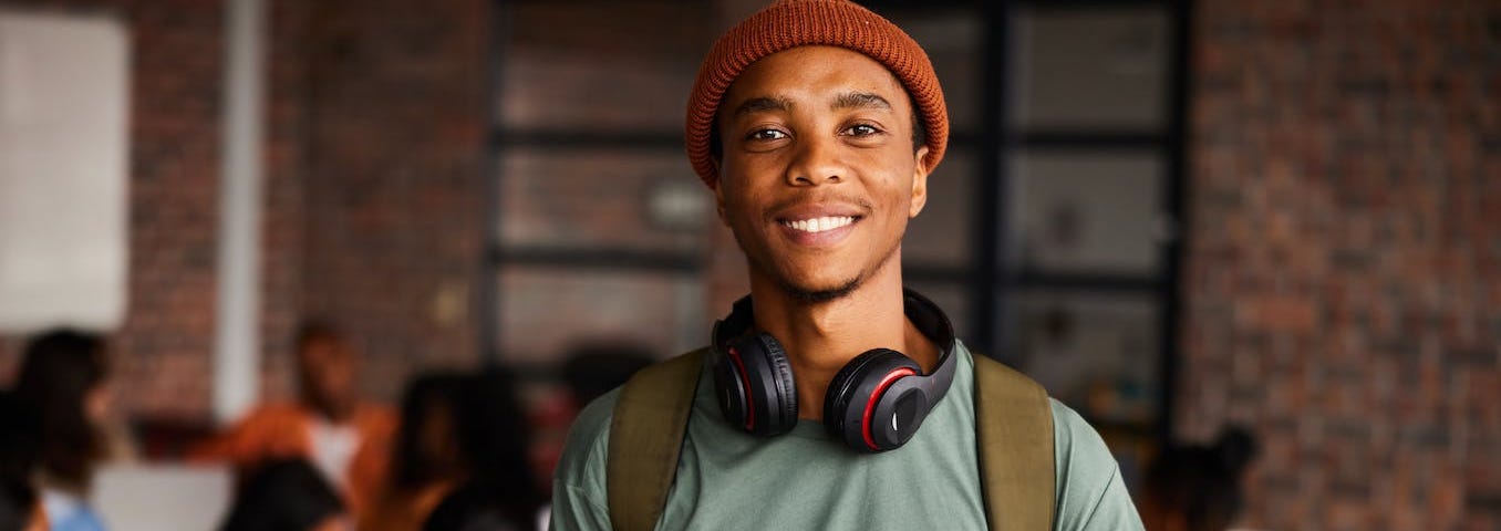 A smiling young man with headphones around his neck, in a classroom