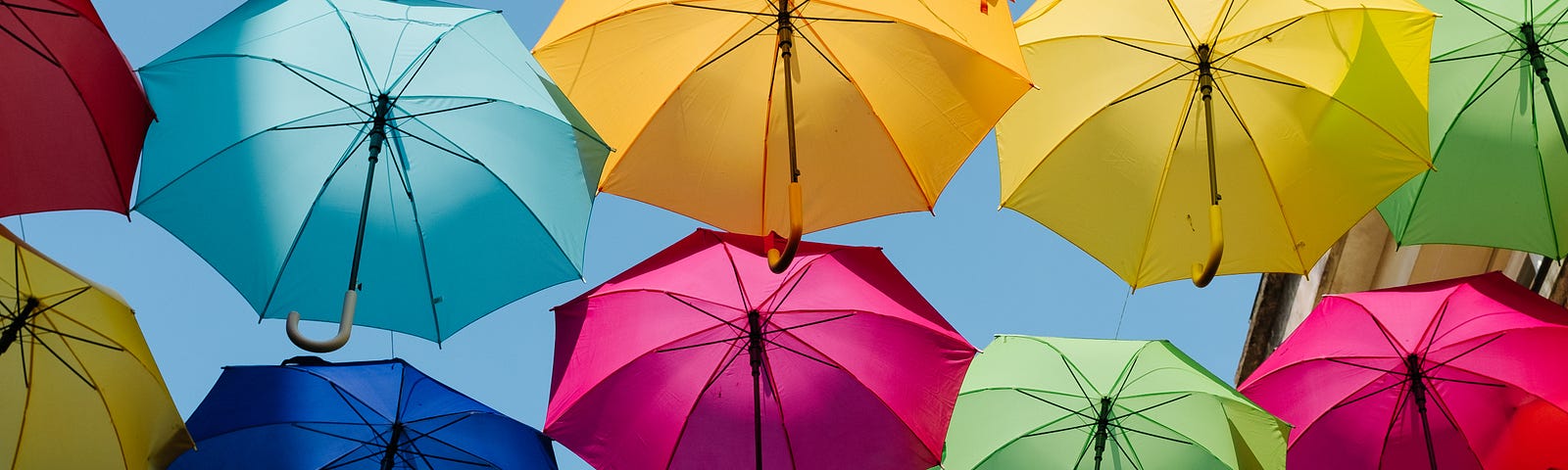 Multiple colorful umbrellas, open against a blue sky.