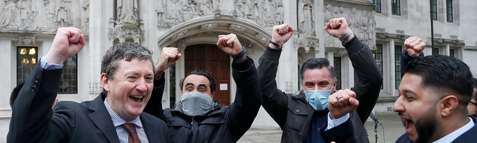 A group of men celebrating outside the London Supreme Court building