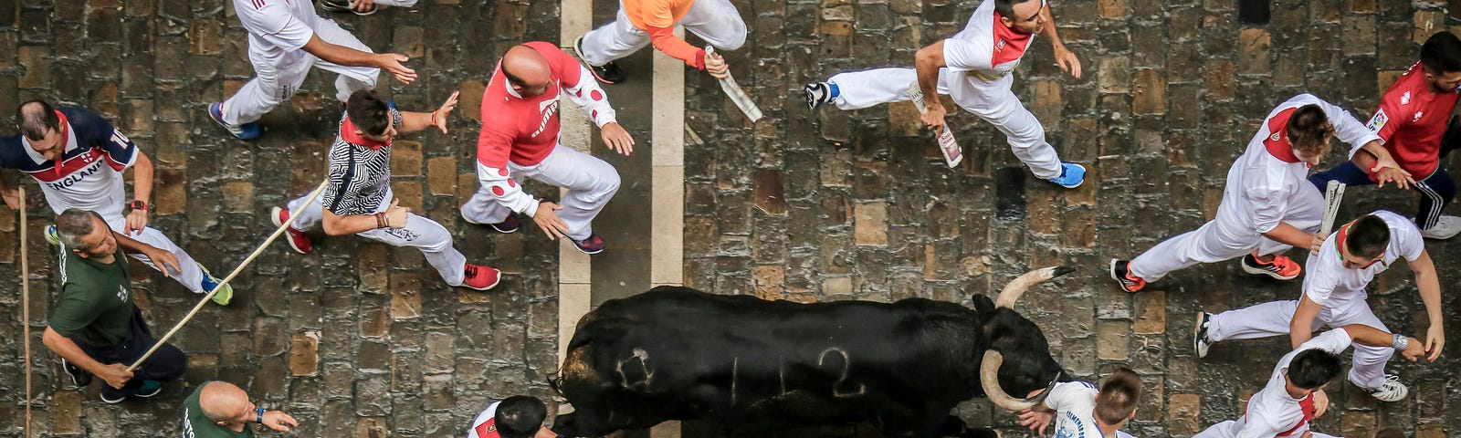 Runners in Pamplona running away from one black bull.