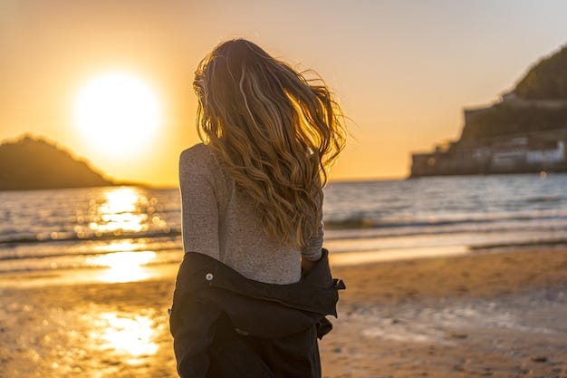 Young woman facing the sunset at the beach