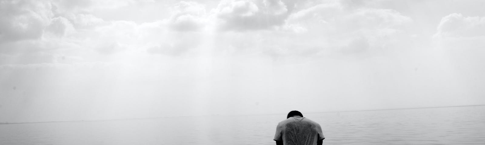 A man stands alone in water, head bowed in sorrow