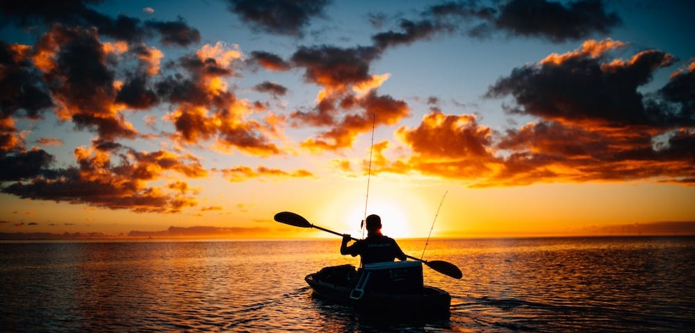 Person paddling canoe at sunset