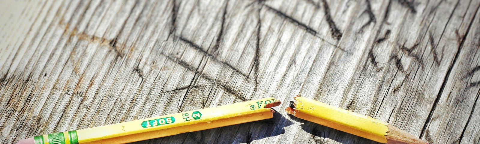 a broken pencil on a wooden table filled with scratch marks