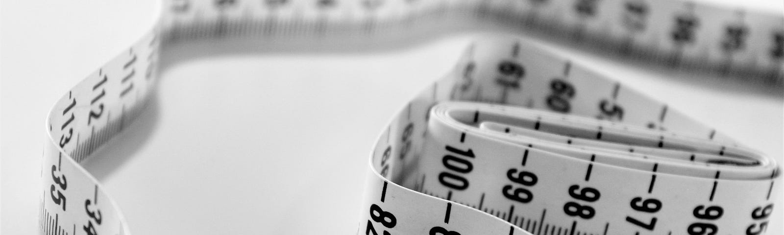 A close-up image of a white measuring tape with black numbers and markings, loosely coiled on a plain surface. The tape is prominently displaying numbers in the 80s and 90s, symbolizing the concept of measurement, tracking progress, or setting goals in various aspects of life.