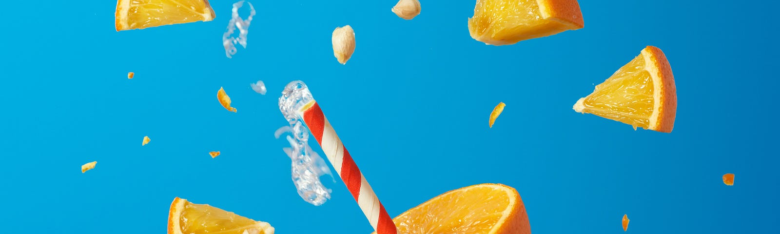 An orange sliced into pieces, with a straw emerging from one. Blue background.