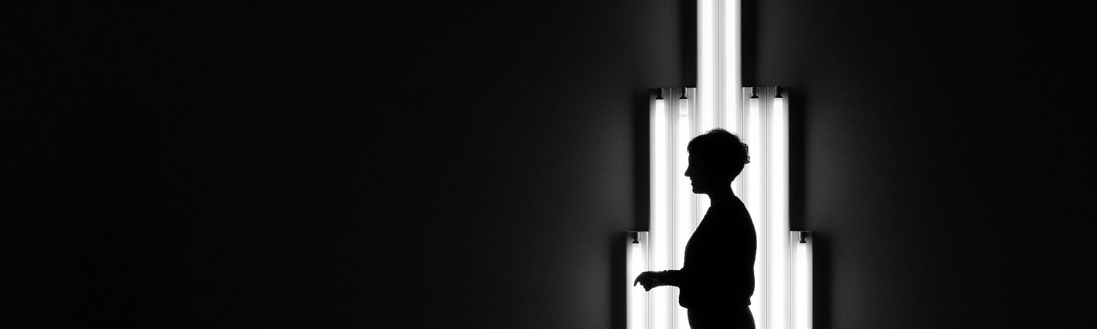 A figure stands silhouetted against an art installation of fluorescent tubes