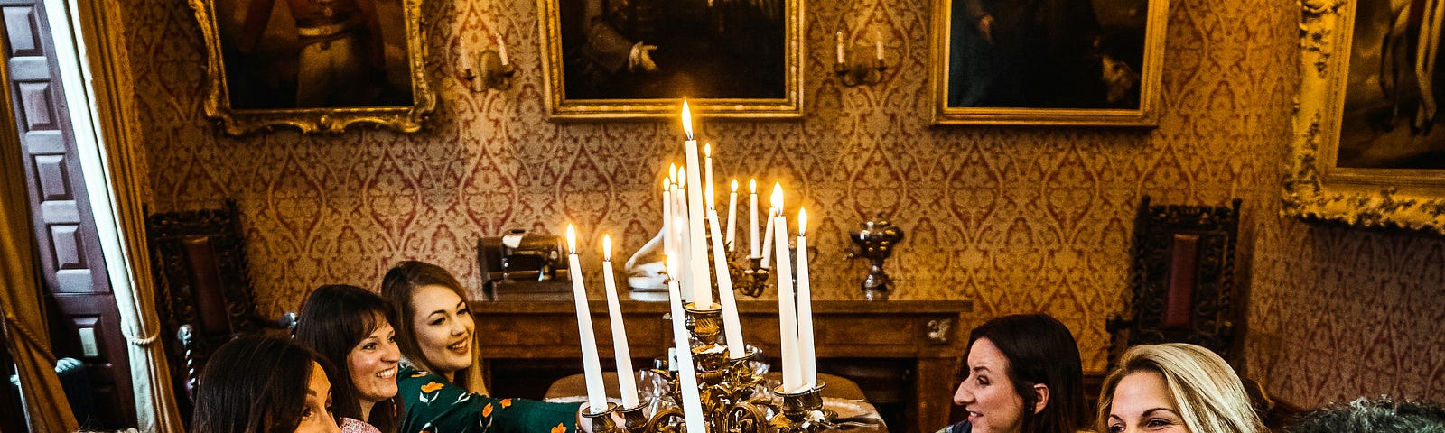 a big group of people sitting around a large table, cheersing each other with drinks with food and candles on the table