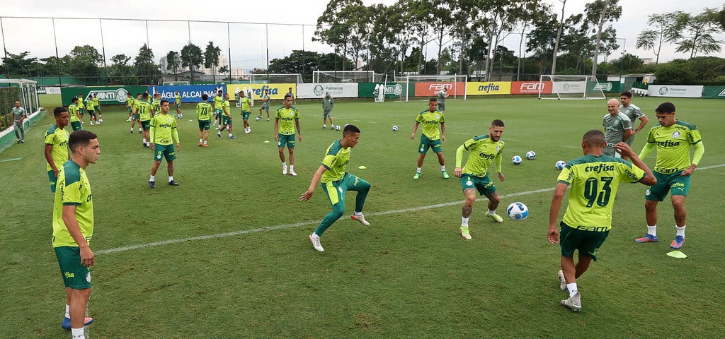 Jogadores do Palmeiras treinam no CT, vestindo camisa verde limão com detalhes em verde escuro, cação verde escuro e meias brancas. há cerca de 20 jogadores na foto, divididos em pequenas rodas e tocando bola