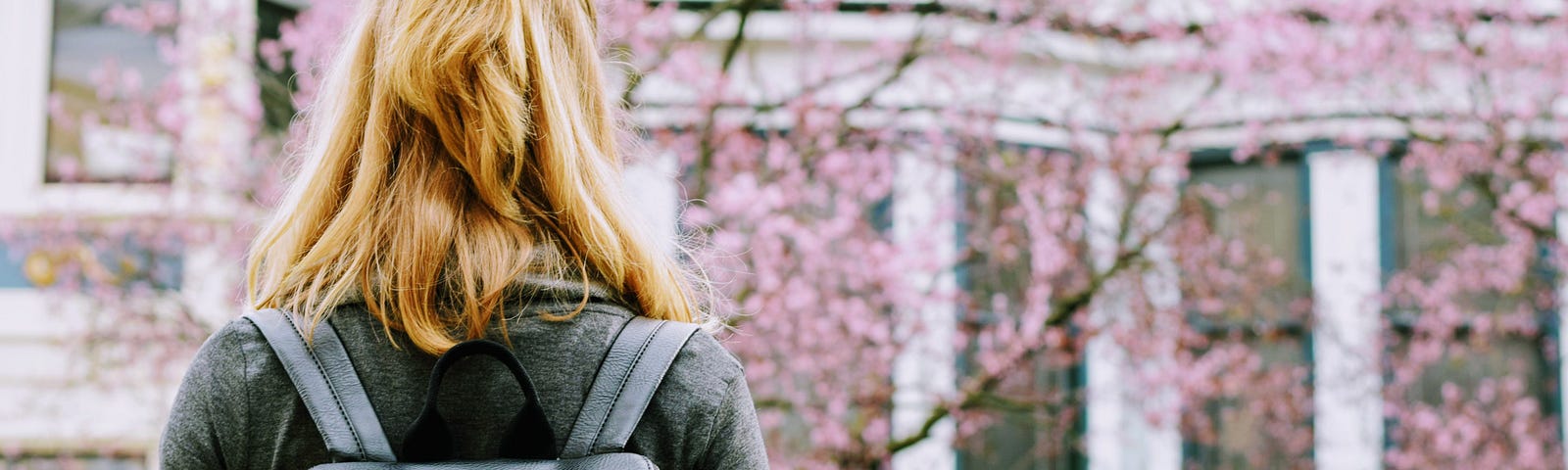 A young woman with a backpack full of books, stands alone facing a building, a university, wondering what is in store for her.