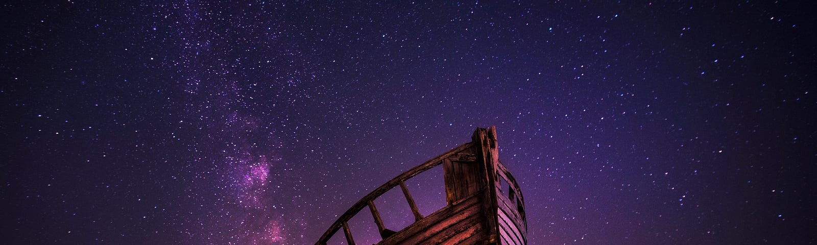 A wooden wreck of a boat under a purple starry sky.