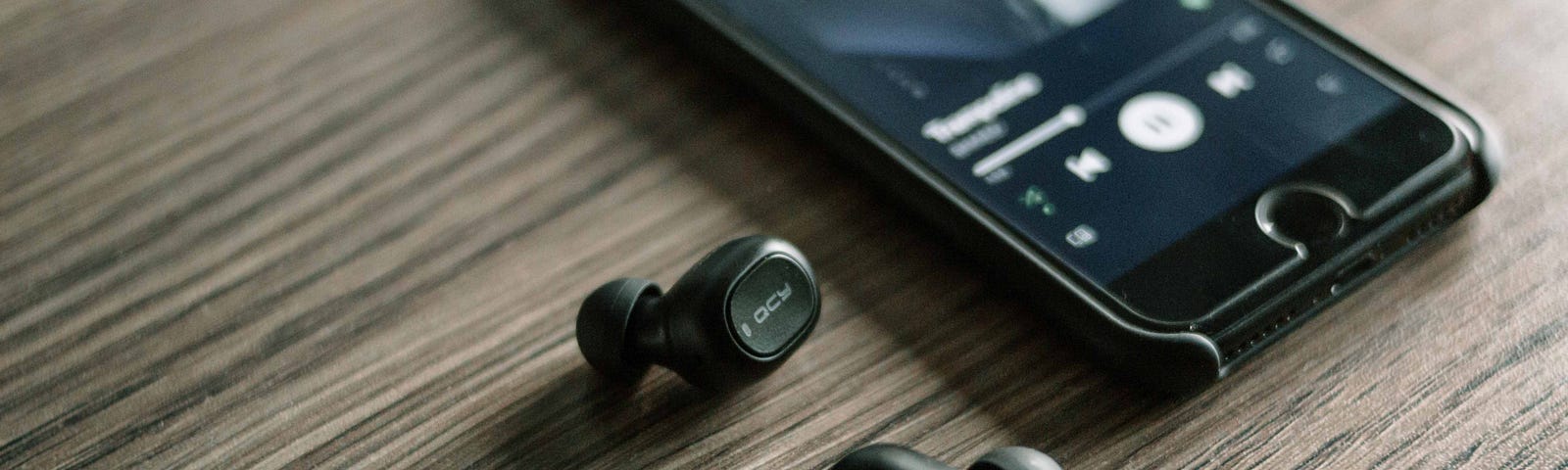 Image of a mobile phone and black earbuds on a wooden surface.