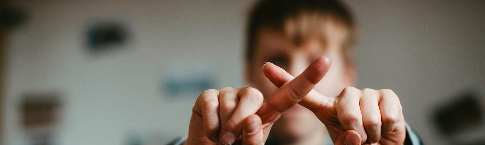 A young kid with a “X’ formed from his two forefingers as a sign of ‘no’.