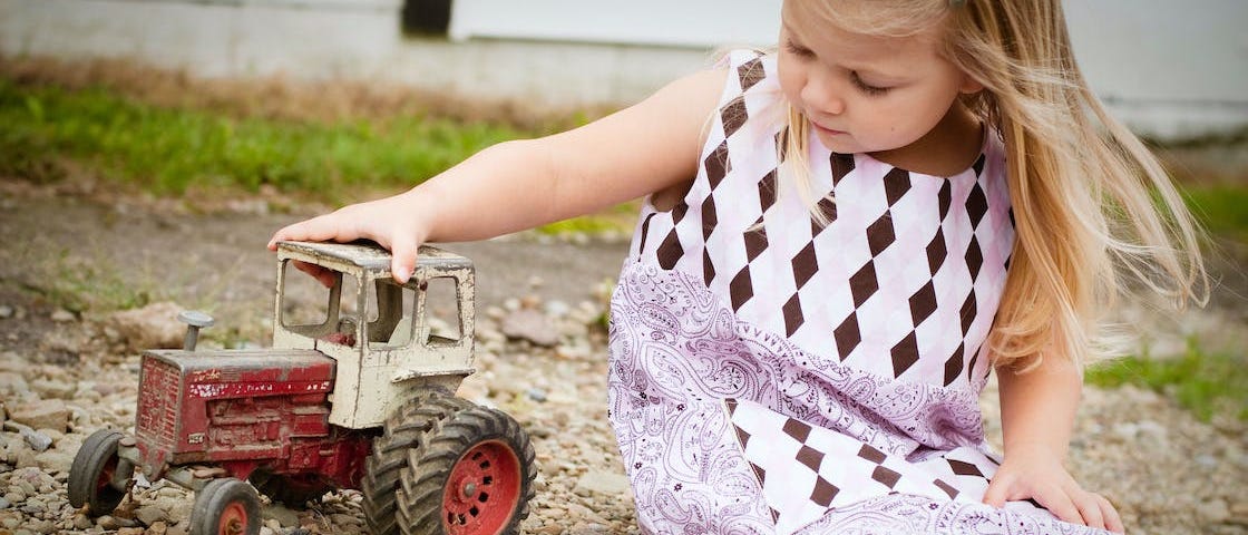 Little girl playing with a toy tractor in the dirt.