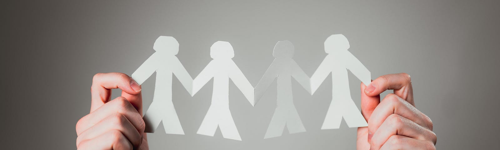 Two hands hold cut out paper figures (humans holding hands).
