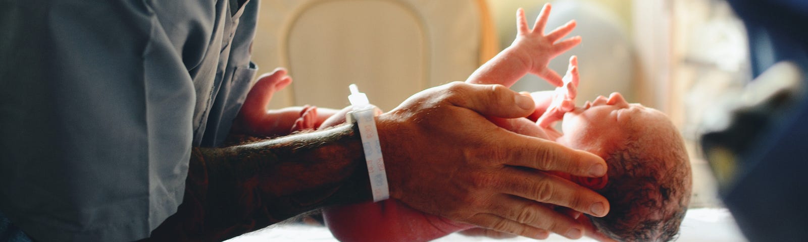 Man’s hands holding newborn over a baby scales.